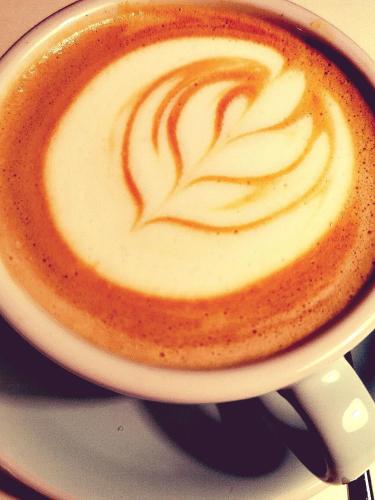 a cup of coffee with a leaf painted on it at Villa Chez les Amis - Adults only in Balatonszepezd
