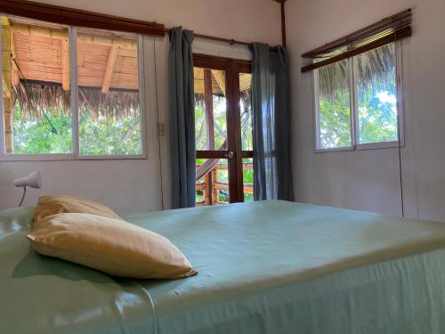 a bed with a pillow on it in a room with windows at Hosteria Guachapeli in Las Tunas