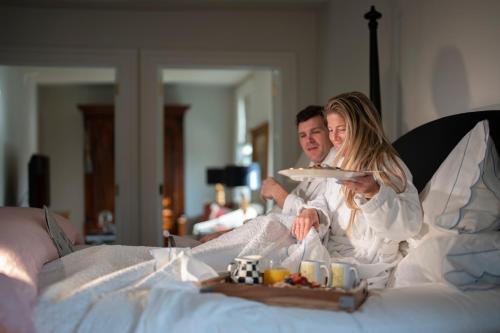 un hombre y una mujer sentados en una cama con un plato de comida en 34 State "Historic Luxury Suites" Skaneateles, en Skaneateles