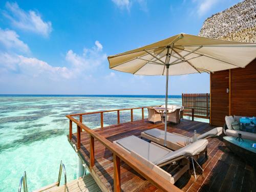 a wooden deck with an umbrella and the ocean at Kandolhu Maldives in Himandhoo 