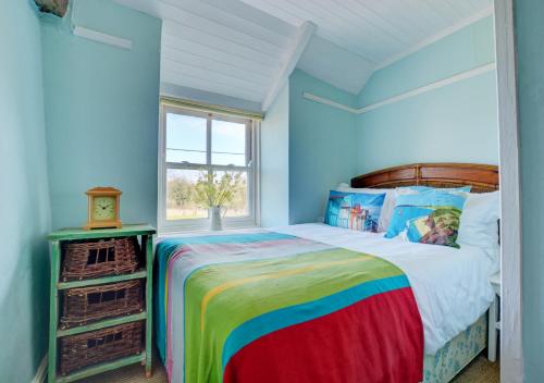 a bedroom with a rainbow bed and a window at Owl Cottage in Little Walsingham