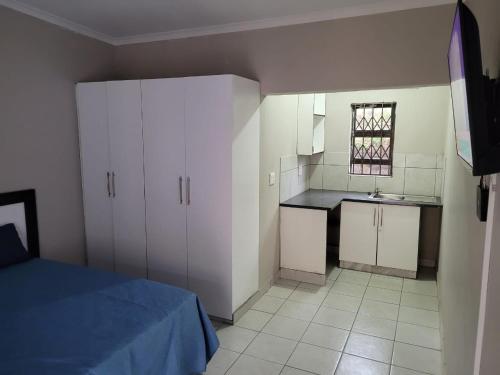 a room with a bed and a kitchen with white cabinets at Mavundla lifestyle lodge in Empangeni