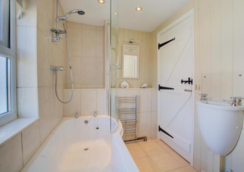 a bathroom with a tub and a shower and a sink at Shamrock Cottage in Hindringham