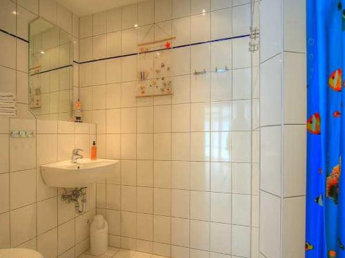 W wyłożonej białymi kafelkami łazience znajduje się umywalka i prysznic. w obiekcie Ferienwohnung Warnemünde w mieście Warnemünde