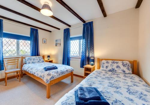 a bedroom with two beds and blue curtains at Tones Cottage in Great Ryburgh