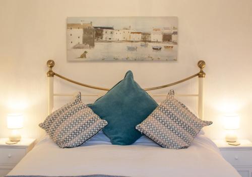 a bed with three pillows and a painting on the wall at Thimble Cottage in Dersingham