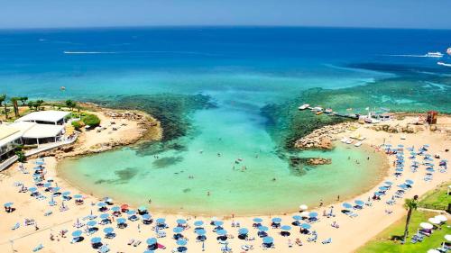 a beach with umbrellas and people in the water at Tsokkos Gardens Hotel in Protaras