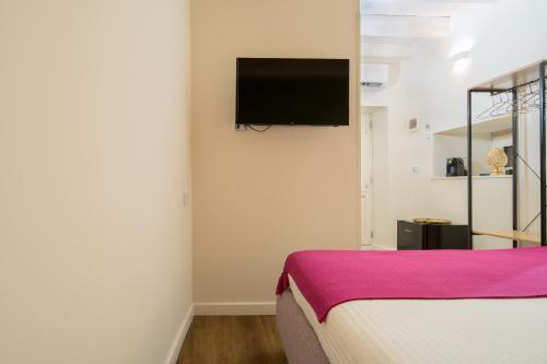 um quarto com uma cama e uma televisão de ecrã plano na parede em The Room Ortigia em Siracusa