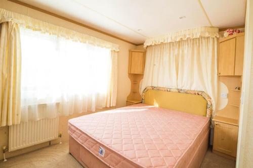 um quarto com uma cama rosa e uma janela em 6 Berth Caravan For Hire With Sea Views At Haven Seashore Ref 22087a em Great Yarmouth