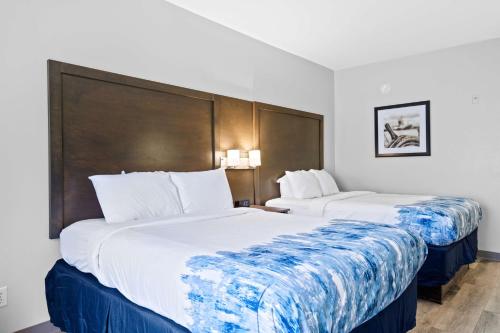 two beds in a hotel room with white and blue sheets at Blue Water Inn & Suites BW Signature Collection in North Topsail Beach