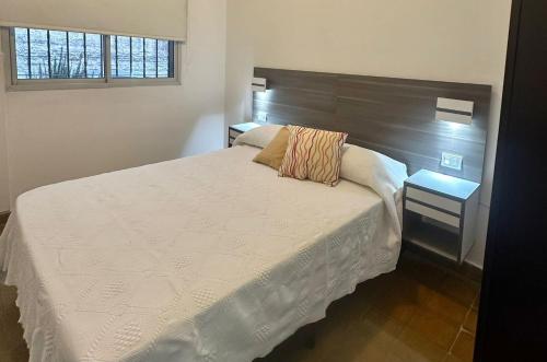 a bedroom with a white bed with a wooden headboard at AMPLIOS Departamentos PASAJE TUCUMÁN in Alta Gracia