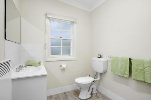 a white bathroom with a toilet and a window at The Teachers Cottage in Mount Wilson