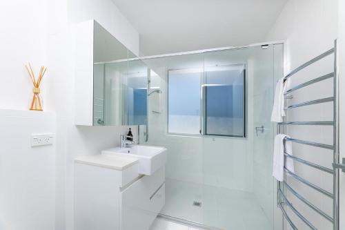 La salle de bains blanche est pourvue d'un lavabo et d'un miroir. dans l'établissement Waterline 303, à Forster