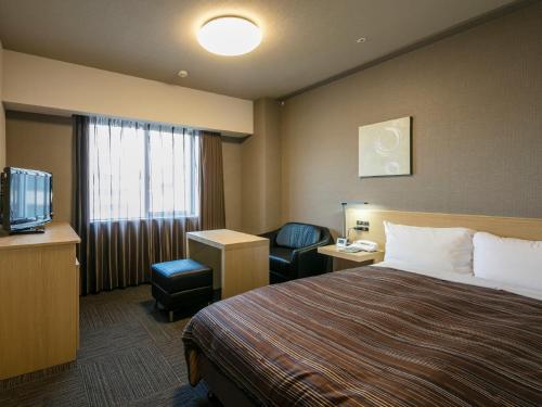 a hotel room with a bed and a chair and a television at Hotel Route-Inn Kumamoto Ekimae in Kumamoto