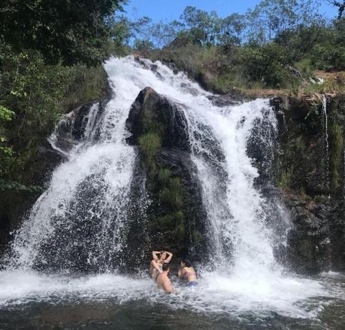 two people in the water in front of a waterfall at Pousada Auroranascerdosol in Manhã
