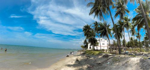 a beach with palm trees and a white building at DIỆP NGỌC MAI Guest House in Mui Ne