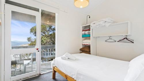 a white bedroom with a bed and a balcony at Shamrock 8 in Mount Hotham