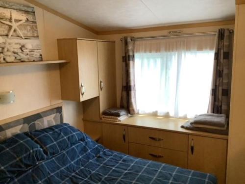 a bedroom with a blue bed and a window at Beautiful 6 Berth Caravan With Wifi In Hampshire Ref 81337sb in Milford on Sea
