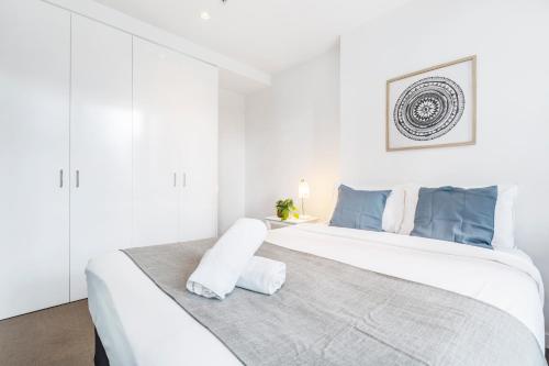 a white bedroom with a large bed with blue accents at Sakura Apartment in Melbourne