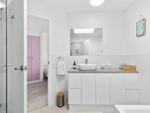 een witte badkamer met een wastafel en een spiegel bij Kawana Beachside Getaway 1 Bedroom Apartment in Buddina