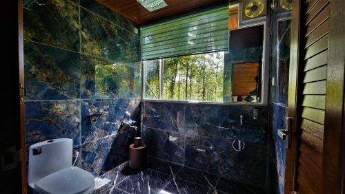 a blue tiled bathroom with a toilet and a window at Coorg Bliss Estate Stay in Madikeri