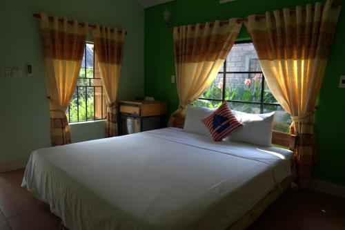 a bedroom with a white bed and two windows at Greenfield Ecostay in Phong Nha