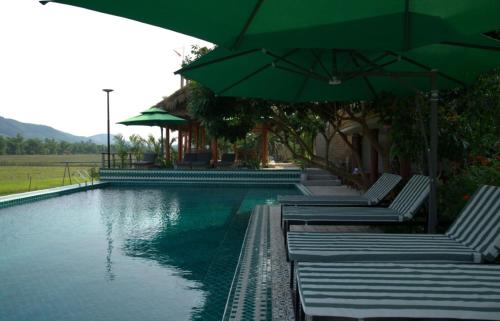 a swimming pool with green umbrellas and lounge chairs at Greenfield Ecostay in Phong Nha