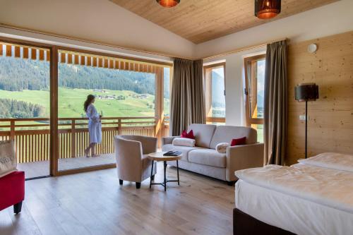 a hotel room with a bed and a woman standing on a balcony at Alpine Nature Hotel Stoll in Valle Di Casies