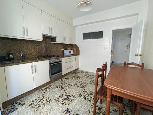 Apartamento Vila Morena في مالبيسا: مطبخ بدولاب بيضاء وطاولة خشبية