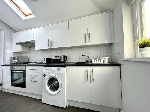 a kitchen with white cabinets and a washing machine at Massive 4 bedroom Duplex Apartment - Sleeps up to 10 People - Free Parking - 5 Minutes to the Best Beach! - Great Location - Fast WiFi - Smart TV - Newly decorated - sleeps up to 10! Close to Bournemouth & Poole Town Centre & Sandbanks in Bournemouth