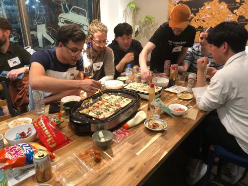 a group of people sitting around a table eating pizza at Guest House Matsu in Osaka