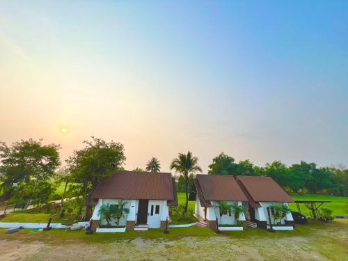 duas casas num campo com o pôr-do-sol ao fundo em The Green Season Resort em Ban Mae Kham Lang Wat