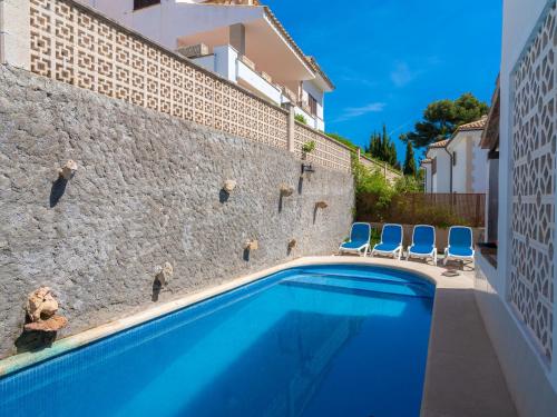 a swimming pool in front of a stone wall with blue chairs at Apartment Clara B - CSV177 by Interhome in Cala de Sant Vicenc