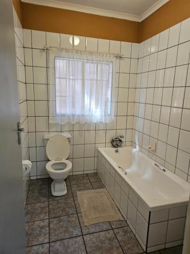 La salle de bains est pourvue de toilettes, d'une baignoire et d'une fenêtre. dans l'établissement Motel Villa Africa, à Polokwane