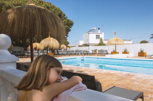 Mała dziewczynka siedząca przy stole przed basenem w obiekcie TAIGA Conil w mieście Conil de la Frontera