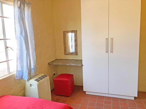 1 dormitorio con armario blanco y taburete rojo en Kalahari Homestead, en Khemsbok
