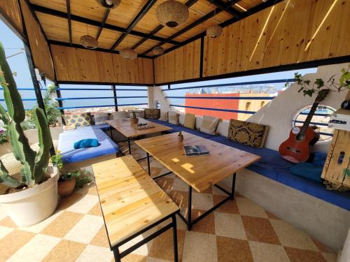 a restaurant with wooden tables and a blue couch at Good Wave Surf House in Tamraght Oufella