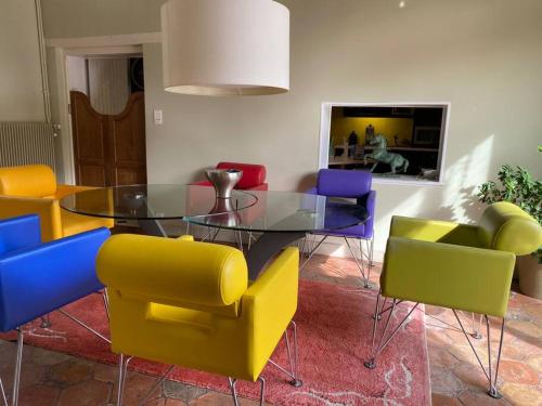 a dining room with a glass table and colorful chairs at Propriété à 3 mins du Château du Haras du Pin in Le Pin-au-Haras