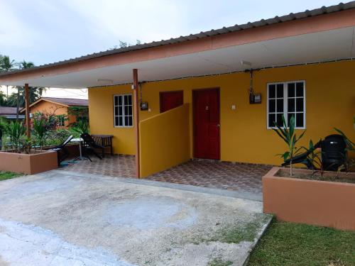 una casa amarilla con puerta roja en Alfa Roomstay en Pantai Cenang