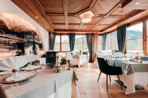 ein Restaurant mit weißen Tischen, Stühlen und Fenstern in der Unterkunft Parkhotel Burgmühle in Fischen im Allgäu