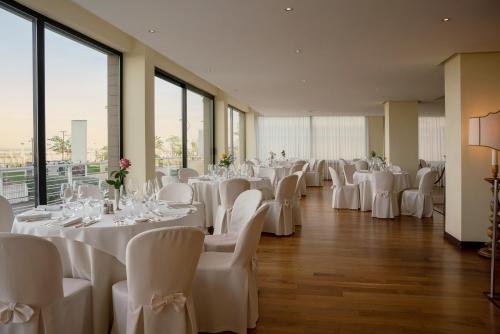 einen Bankettsaal mit weißen Tischen, Stühlen und Fenstern in der Unterkunft National Hotel in Rimini