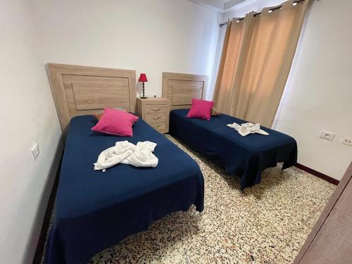 Duas camas num quarto com lençóis azuis e almofadas cor-de-rosa em Apartamento Canarias em Los Cristianos
