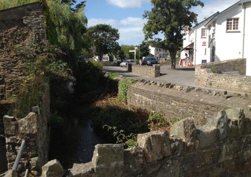 a river next to a stone wall next to a street at Beren in Croyde