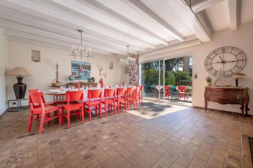une salle à manger avec des chaises rouges, une table et une horloge dans l'établissement Villa avec jacuzzi - 15 pers. à 350m de la plage, à Saint-Brévin-les-Pins