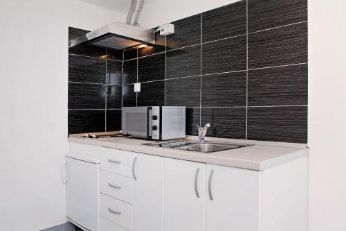 a kitchen with white cabinets and a sink and black tiles at Apartments Park in Vela Luka