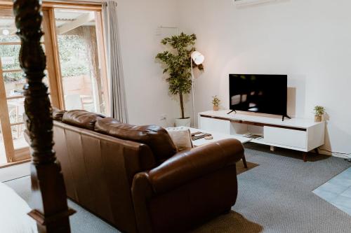 sala de estar con sofá de cuero marrón y TV en The Garden Suite, en The Patch