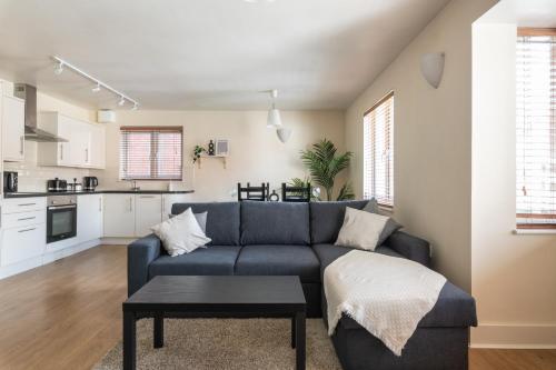 a living room with a blue couch and a kitchen at Spacious 2BR Flat - 2 Free Parking Spaces - Near LGW Airport in Crawley
