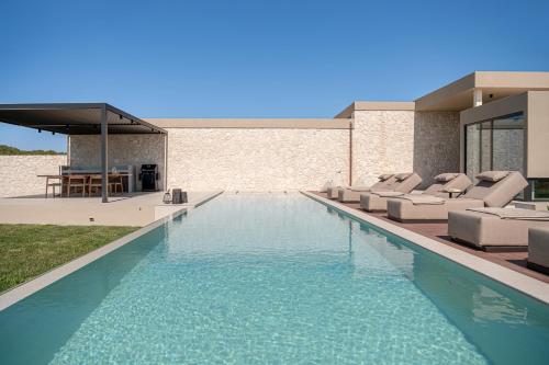 a swimming pool with lounge chairs and a house at Pnoe Villas - Seafront Experience in Tavronitis