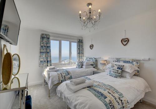 two beds in a white room with a chandelier at The Farthings in Ilfracombe