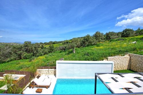 a swimming pool with white chairs and a hill at Villa Silentium Ionia by PosarelliVillas in Aryiroúpolis